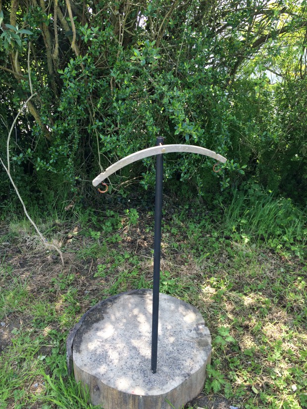 Wooden coat hanger attached to pole, with cup hooks attached on either end to make garden weighing scale